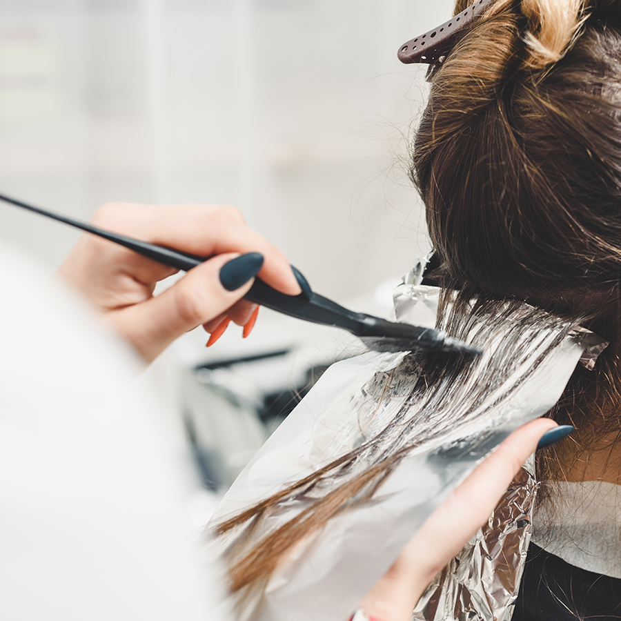 Young professional hairdresser applying dye on clients hair